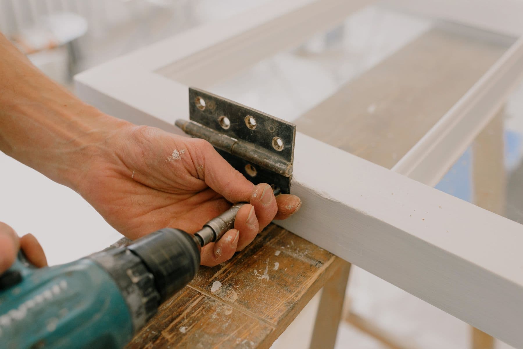 Hands fitting a hinge to a white door with a cordless drill
