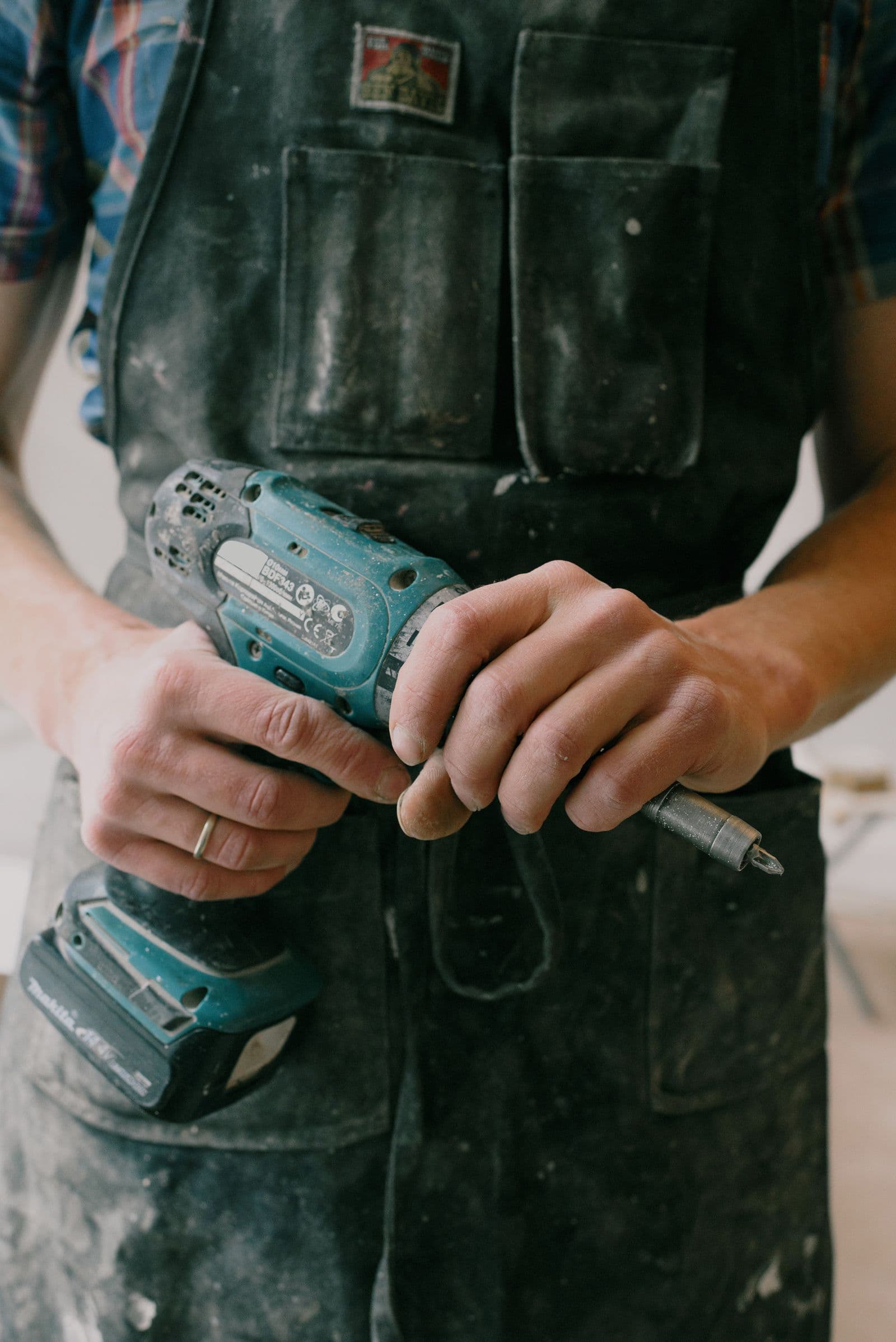 Tradesman holding a cordless drill in a dust-covered work apron