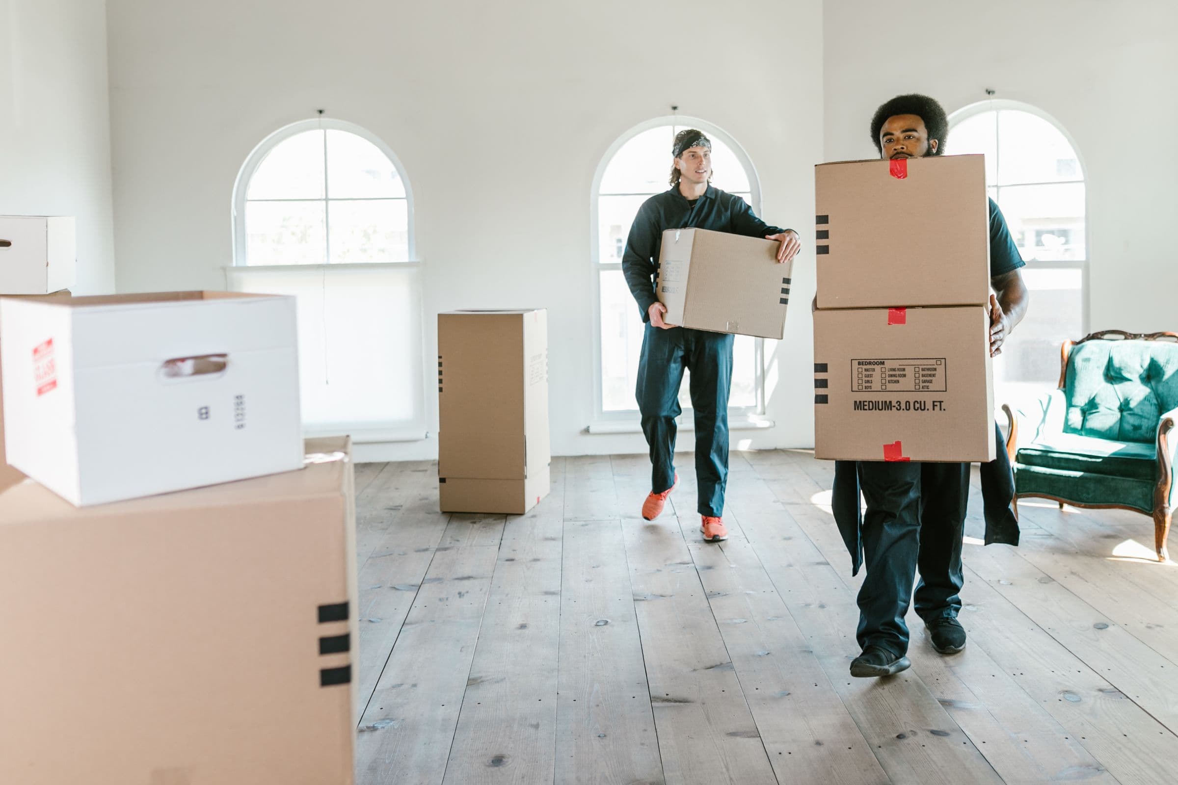Two movers carrying boxes through a bright empty room