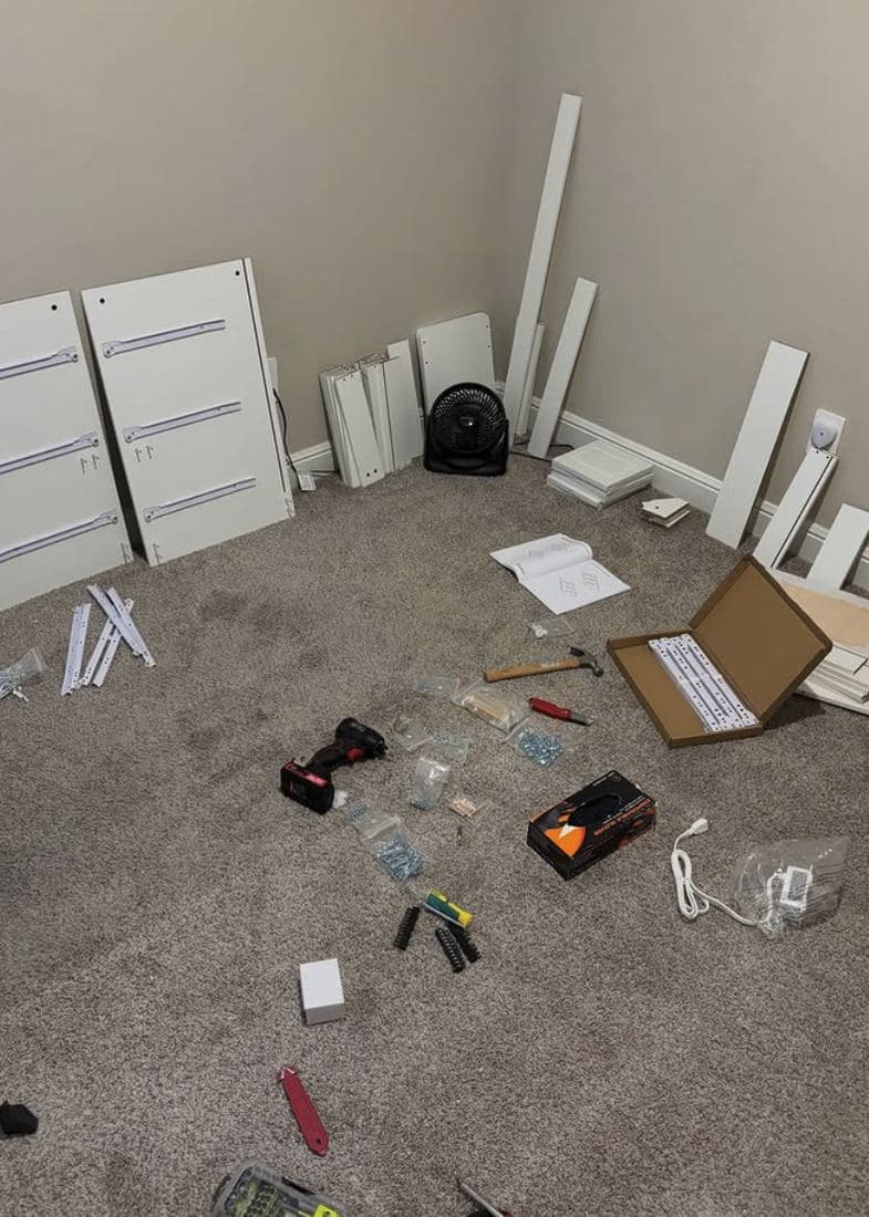 Flat-pack furniture parts and tools laid out in order across a bedroom floor